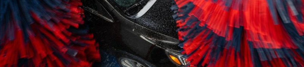 A black car going through a Mark VII car wash with red and blue striped rollers scrubbing the car.