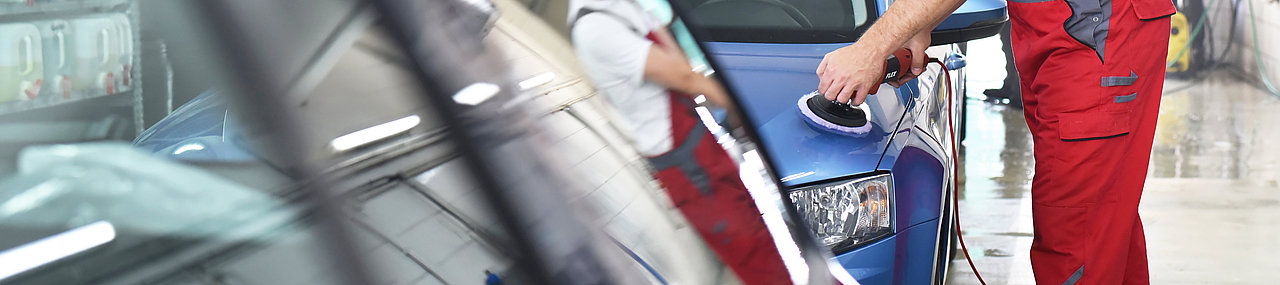 A car wash employee wearing red overalls washing a car at a dealership.