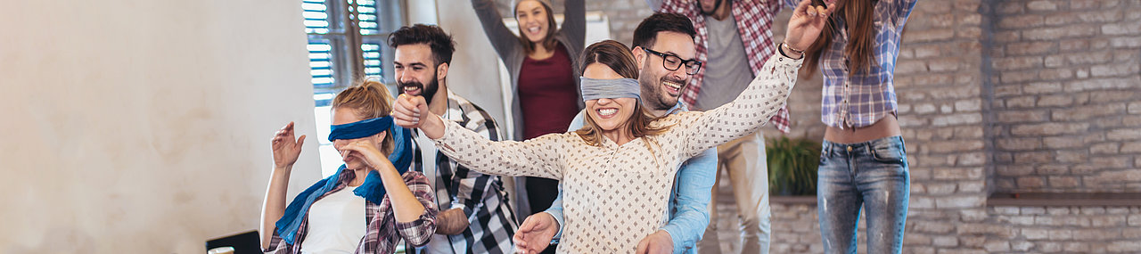 A group of friends cheering on their competing friends wearing blind folds.