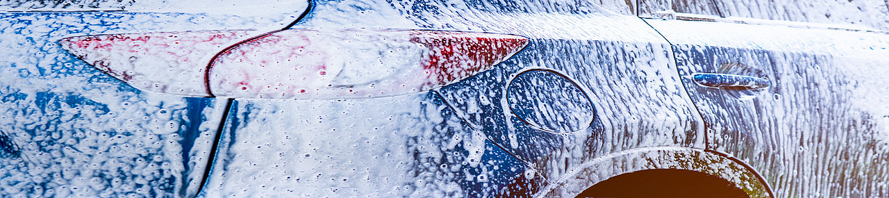 View from the back of a blue car covered in car wash chemicals.