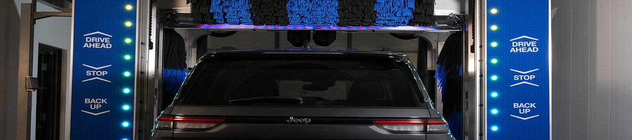 A black crossover driving through a blue Mark VII ChoiceWash with black and blue stripped control arms cleaning the car.