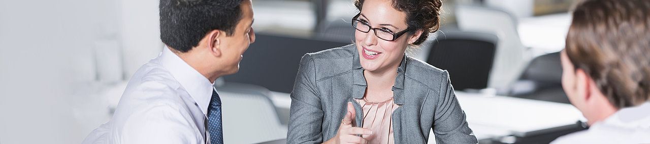 A woman in a grey suit telling two men in white button down shirts the options that they have available to them in a meeting.
