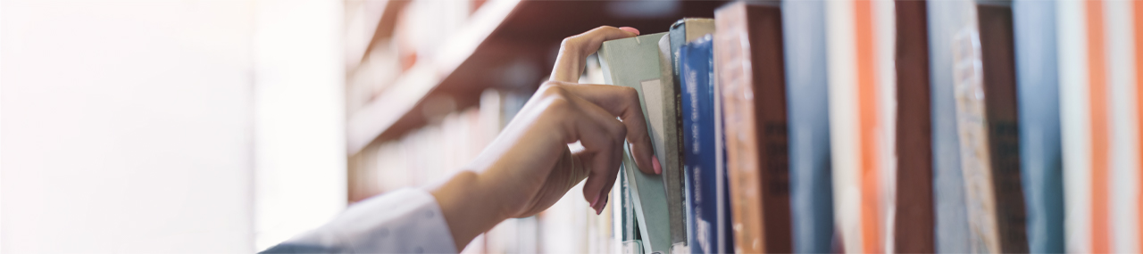A hand pulling a book off of the shelf on a sunny day.