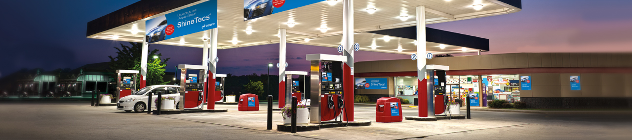 A gas station lit up at night with ShineTec chemical advertisements on the wall.