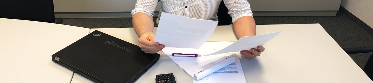 Man filling out paper work with a computer in front of him that says WashTec.