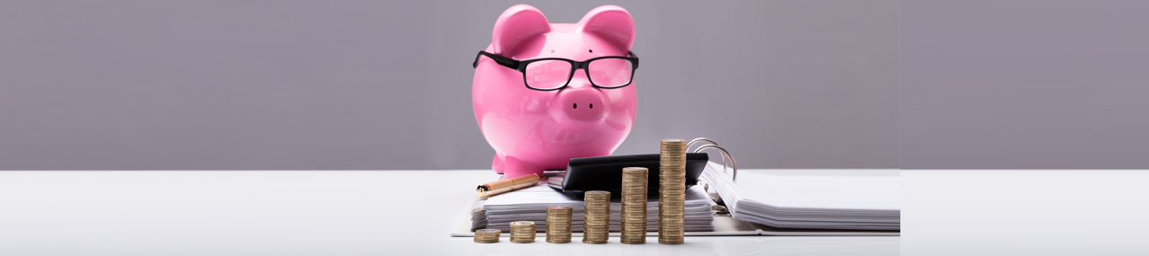 A pink piggy bank wearing glasses doing finances surrounded by money.
