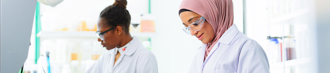 2 women in white lab coats and glass checking the Mark VII chemical compliance.