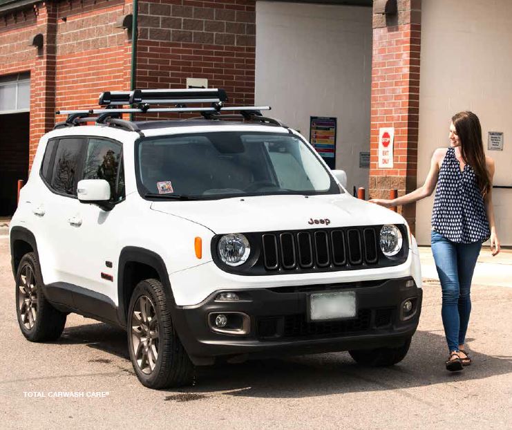 Woman with brown hair, black shirt, and jeans standing next to a clean white Jeep after getting out of a Mark VII in bay automatic car wash in Colorado.